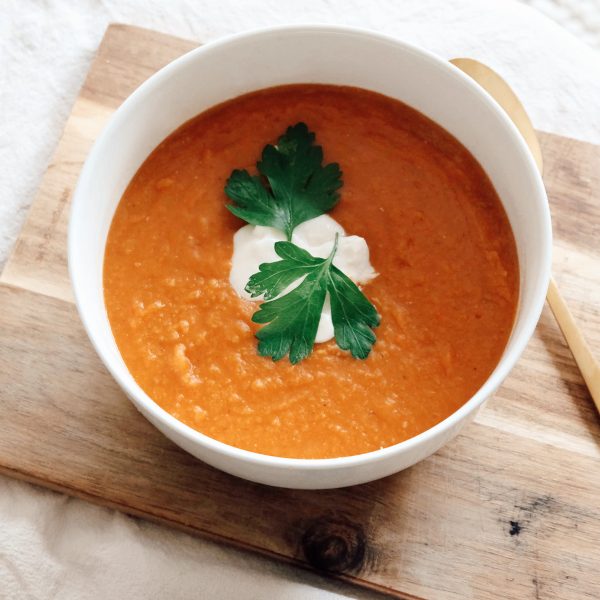 Red lentil soup garnished with parsley and yoghurt in a ceramic bowl with a golden spoon