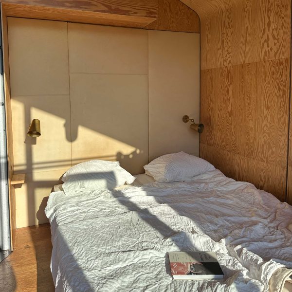 Cozy wooden cabin interior with white bedding, wood-paneled walls, and a book on the bed
